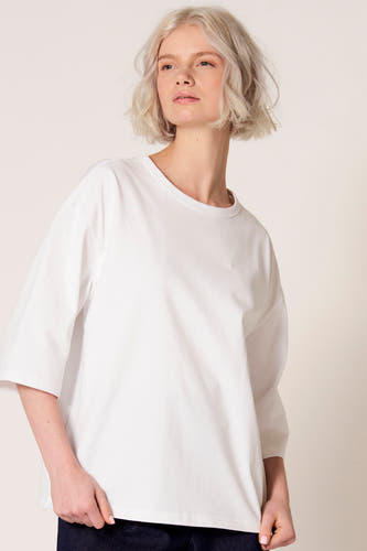 T-shirt blanc à manches courtes de Clouds of Fashion, porté avec un pantalon foncé.
