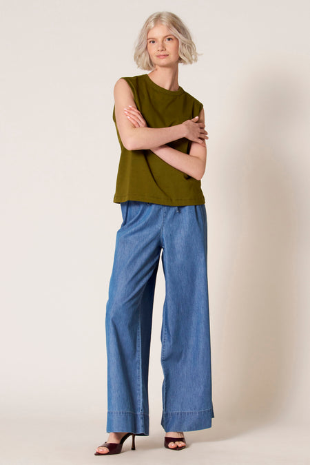 Mouwloze groene singlet van Clouds of Fashion, gedragen met wijde denim broek en hakken.
