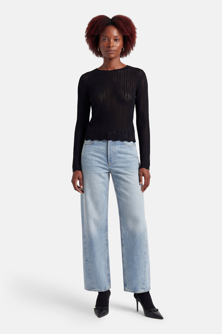 T-shirt noir à manches longues de HAILYS, avec un motif en maille transparente et associé à un jean ample et des escarpins noirs.
