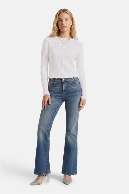 T-shirt blanc à manches longues de HAILYS, avec un motif au crochet, combiné avec un jean bleu et des talons argentés.