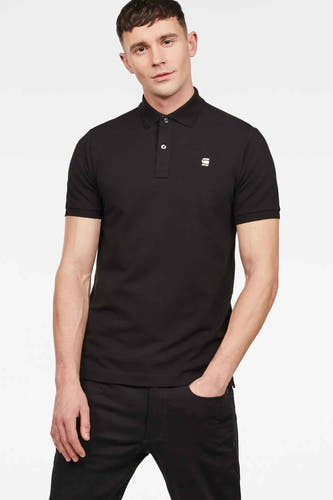 Polo noir de G-Star RAW, porté par un homme avec une main dans sa poche, associé à un pantalon noir.