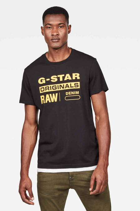 T-shirt noir de G-Star RAW avec des logos de marque jaunes et porté avec un pantalon vert.