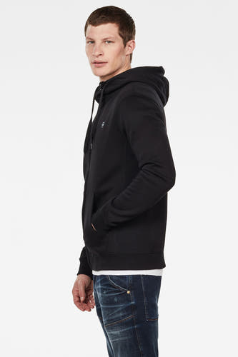 Gilet noir G-Star RAW, avec capuchon et poches, porté sur un chemisier blanc et un jean bleu, en vue de profil.