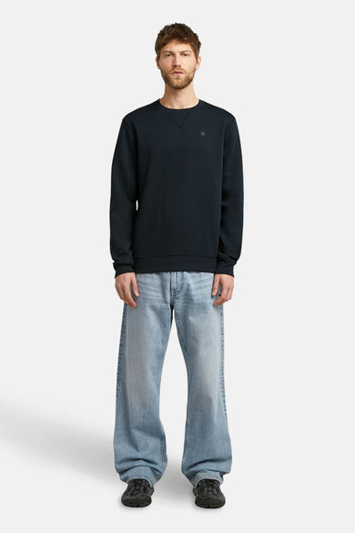Pull-over bleu avec col rond de G-Star RAW, porté avec des jeans larges et des baskets noires.
