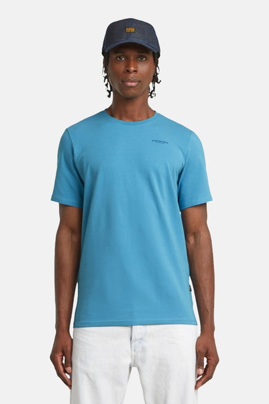 T-shirt bleu à manches courtes de G-Star RAW, porté avec un chapeau et un pantalon blanc.