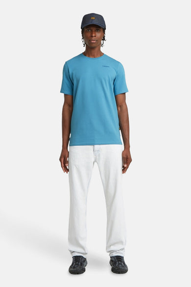 T-shirt bleu à manches courtes de G-Star RAW, avec une petite impression sur la poitrine, associé à un jean blanc et un chapeau.