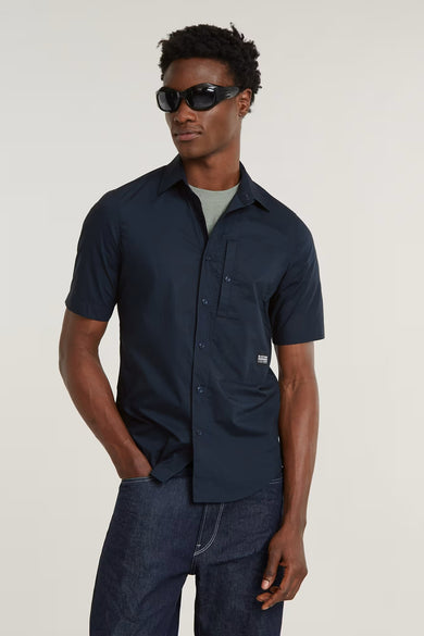 Chemise noire à manches courtes de G-Star RAW, avec poche poitrine et portée avec un T-shirt gris et un jeans foncé.