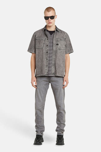 Chemise de jeans grise de G-Star RAW, portée sur un t-shirt rayé, avec des jeans coordonnés et des baskets noires.