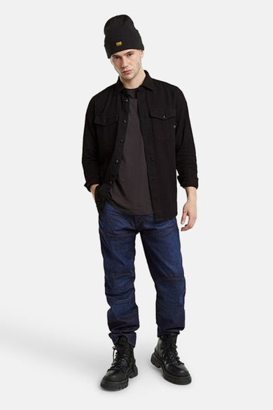 Grijs hemd met lange mouwen van G-Star RAW, gedragen over een grijs T-shirt, gecombineerd met donkerblauwe jeans en zwarte laarzen.

