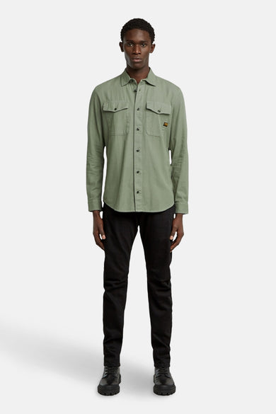 Chemise verte à longues manches de G-Star RAW, avec deux poches po torse et un pantalon noir et des chaussures.