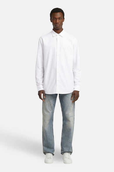 Blouse blanche à manches longues de G-Star RAW, portée avec des jeans et des baskets blanches.