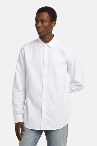 Chemise blanche à manches longues de G-Star RAW, portée avec des jeans bleus.