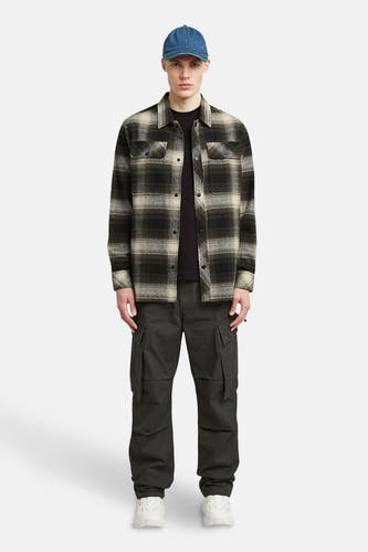Veste verte de G-Star RAW, avec un motif rayé, portée sur une chemise noire et des pantalons cargo foncés et un chapeau bleu.