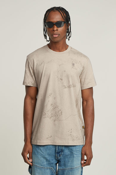 T-shirt beige à manches courtes de G-Star RAW, avec une subtile impression crackle et porté avec des jeans bleus.