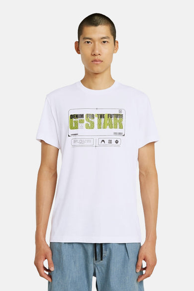 T-shirt blanc à manches courtes de G-Star RAW, avec une impression sur la poitrine, associé à des jeans bleus décontractés et des chaussures noires.