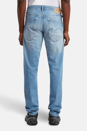 Jean tapered de denim bleu clair G-Star RAW, avec une vue arrière avec des poches et des chaussures noires.