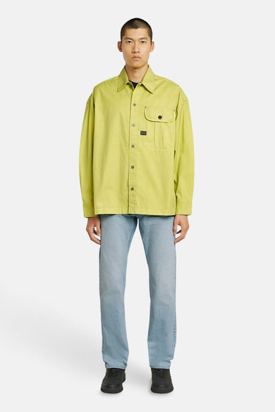 Chemise verte à manches longues de G-Star RAW, avec une poche sur la poitrine, portée avec un jean et des chaussures noires.