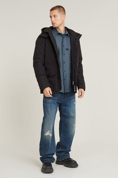 Veste longue noire de G-Star RAW portée sur un chemisier rayé bleu et des jeans déchirés.