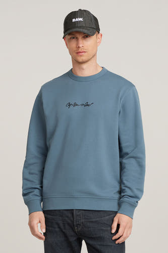 Blauwe sweater met ronde hals van G-Star RAW, met een klein logo op de borst en donkere jeans.
