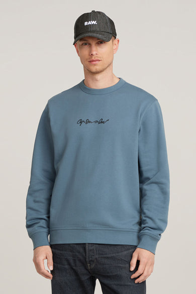 Pull bleu à col rond de G‑Star RAW, avec un petit logo sur la poitrine et jean foncé.