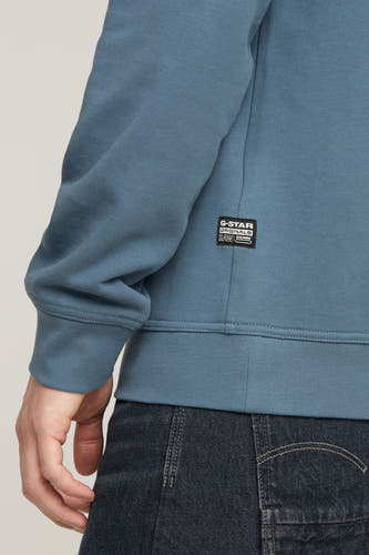 Blauwe sweater van G-Star RAW, met een labeldetail op de zijkant, gedragen met donkere jeans.
