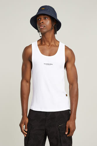 Witte singlet van G-Star RAW, gedragen met een donkerblauwe hoed en camouflagebroek.
