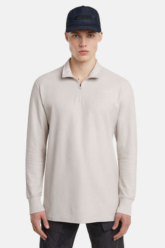 Gilet écru de G-Star RAW avec un col à fermeture éclair et des manches longues, porté avec une casquette bleu foncé.