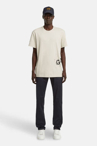 T-shirt écru à manches courtes de G-Star RAW, avec une impression noire et porté avec un pantalon foncé et des baskets blanches.