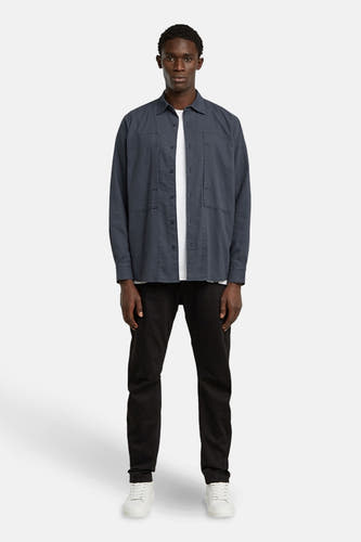 Chemise bleue à manches longues de G-Star RAW, portée sur un T-shirt blanc avec des jeans noirs et des baskets blanches.
