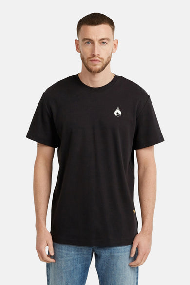 T-shirt noir de G-Star RAW avec un petit logo blanc sur la poitrine, porté avec des jeans bleus.