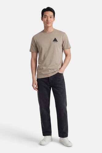 Grijs T-shirt met korte mouwen van G-Star RAW, met een driehoekig logo op de borst, gecombineerd met donkere jeans en witte sneakers.
