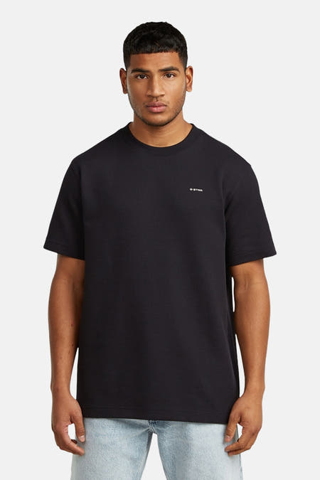 T-shirt noir à manches courtes de G-Star RAW, porté avec un jean bleu clair et des chaussures en cuir noires.