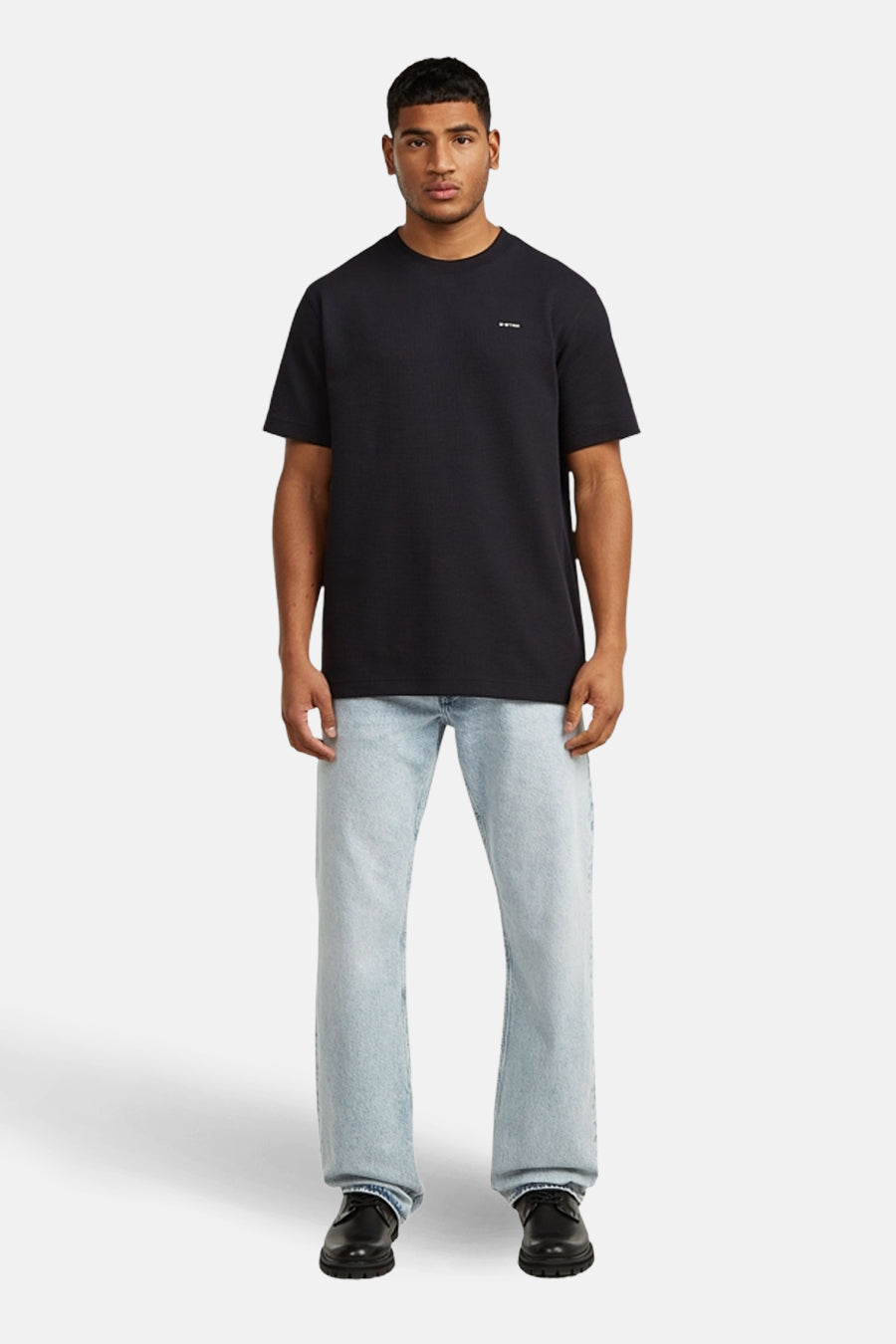 T-shirt noir à manches courtes de G-Star RAW, avec un petit logo sur la poitrine, combiné avec un jean bleu clair et des chaussures noires.