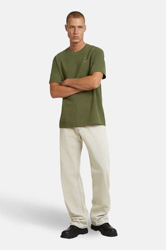 T-shirt vert à manches courtes de G-Star RAW, avec un logo brodé, porté avec un jean ample de couleur crème et des chaussures noires.
