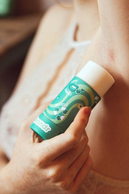 Bâton de déodorant vert - gingembre et citron de WONDR CARE, utilisé par une femme, avec des symboles 'aime-toi' et de recyclage.