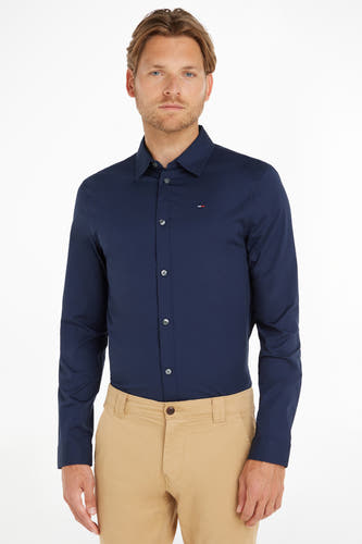 Chemise bleue à manches longues de TOMMY JEANS, avec col boutonné, portée avec un pantalon kaki.
