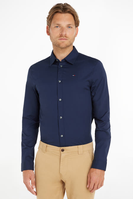 Chemise bleue à manches longues de TOMMY JEANS, avec col boutonné, portée avec un pantalon kaki.