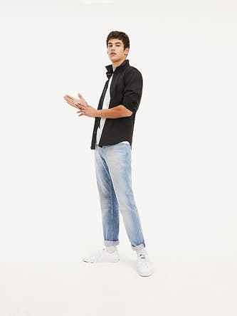 Chemise noire à manches longues de TOMMY JEANS, portée sur un T-shirt blanc, avec des jeans bleus et des baskets blanches.