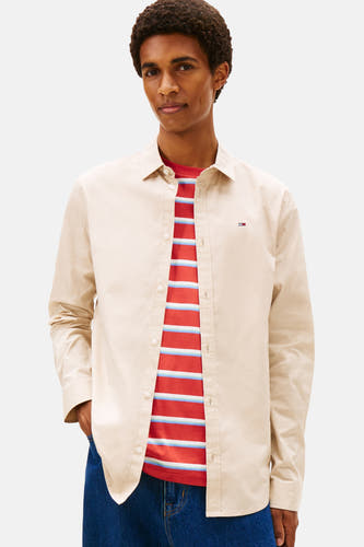 Chemise beige à longues manches de TOMMY JEANS, portée sur un t-shirt rayé et des jeans larges.