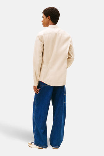 Chemise beige à longues manches de TOMMY JEANS, vue de derrière, avec des jeans bleus délavés et des baskets.