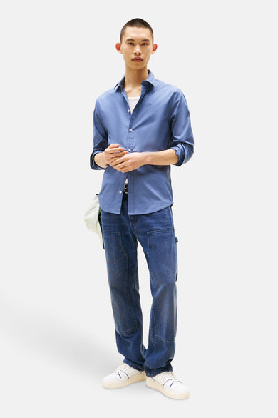 Chemise bleue à manches longues de TOMMY JEANS, avec un col ouvert et des poignets boutonnés, portée sur une chemise blanche.
