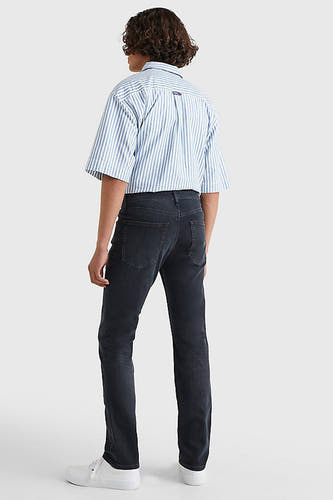 Donkergrijze slim fit jeans van TOMMY JEANS, gecombineerd met een blauw gestreept overhemd en witte sneakers, gezien van achteren.