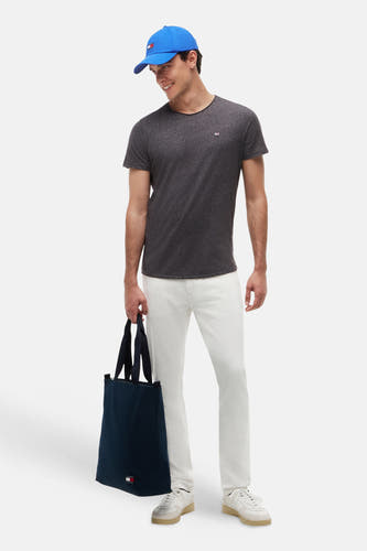 T-shirt noir chiné de TOMMY JEANS, col rond, avec petit logo sur la poitrine, porté dans un look lifestyle avec un pantalon blanc et une casquette bleue
