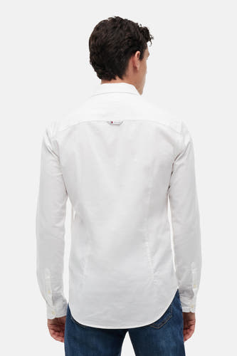 Chemise blanche à manches longues de TOMMY JEANS, vue de dos d'un homme, avec petit logo TOMMY JEANS sur le empiècement dos et jean bleu.
