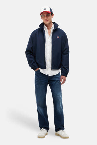 Chemise blanche à manches longues de TOMMY JEANS, portée sous une veste bleu marine, un jean et une casquette.