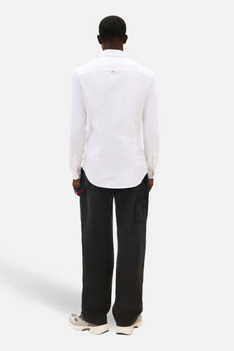Chemise blanche à manches longues de TOMMY JEANS, portée avec un pantalon noir et des chaussures grises, vue de dos.