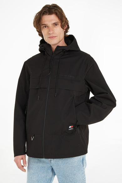 Veste courte noire à capuche de TOMMY JEANS, avec fermeture éclair, poches et écusson logo, vue de face sur un mannequin portant un jean bleu clair