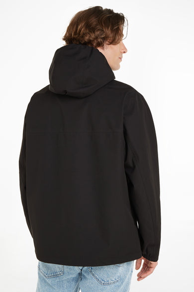 Veste courte noire à capuche de TOMMY JEANS, vue de dos, tissu lisse, le modèle porte un jean bleu clair