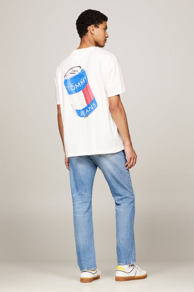T-shirt écru à manches courtes de TOMMY JEANS, avec un imprimé bouteilles sur le dos, associé à des jeans bleus et des baskets blanches.