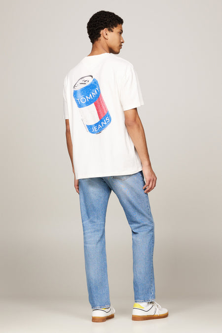 T-shirt écru à manches courtes de TOMMY JEANS, avec un imprimé bouteilles sur le dos, associé à des jeans bleus et des baskets blanches.